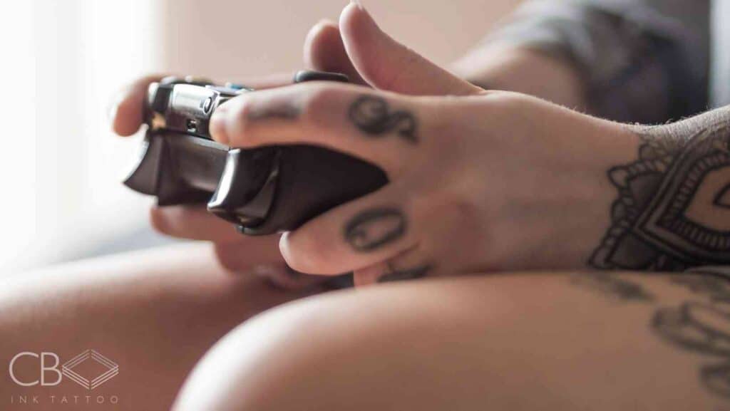 Video Game Tattoos A Celebration of Pixels, Nostalgia, and Art Someone Holding Video Controller Tattooed Hands Tattooed Legs Blog Cover Image