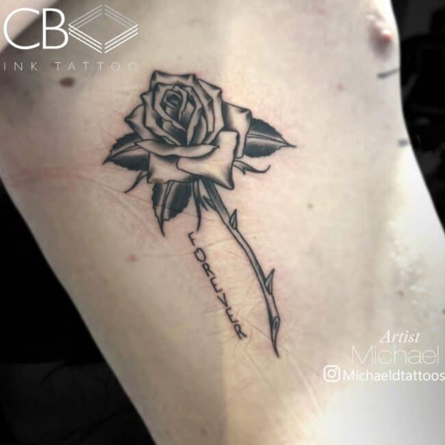 Michael Tattoo Artist Fine Line Black and Grey Rose with Thorns Writing Vertical Forever Rib Tattoo