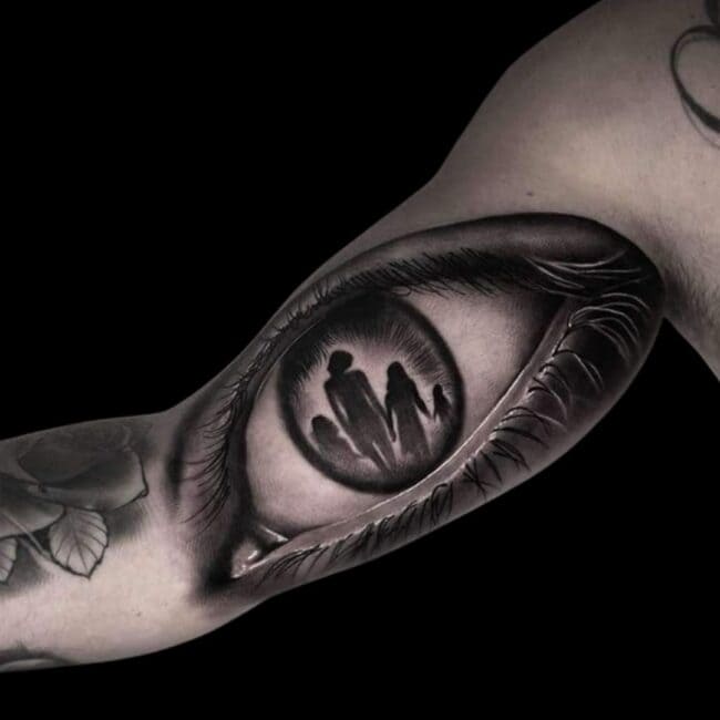 Penno Tattoo Artist Realism Black and Grey Detailed Eye Eyelashes with Woman and Three Children Silhouettes In Iris and Pupil Area Inner Bicep Tattoo