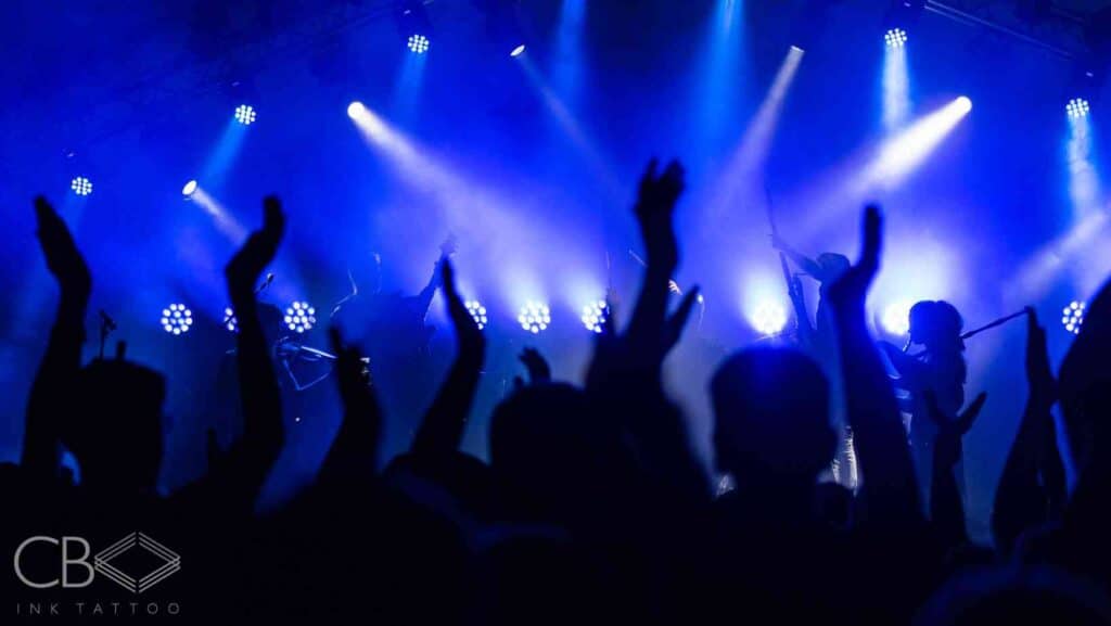Pioneers of Ink Musicians Who Pushed Tattoo Culture Forward Colour Photo of Crowd Hands in front of Stage Lights Music Band Blog Cover Image