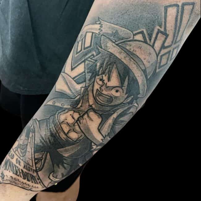Rhys Tattoo Artist Anime Cartoon Black and Grey One Piece Luffy In Dramatic Pose Wanted Poster Japanese Writing In The Background Forearm Tattoo