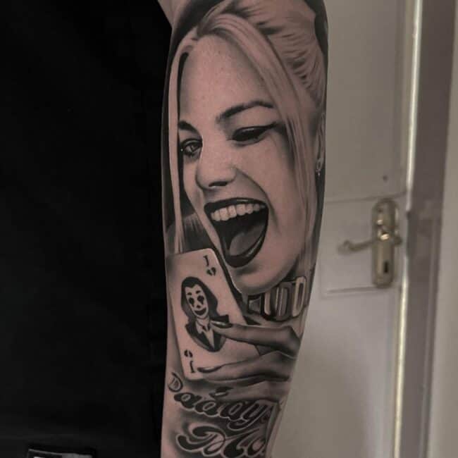 Black and grey Realism Portrait Harley Quinn Margot Robbie Winking Holding Joker Card Arm Sleeve Tattoo