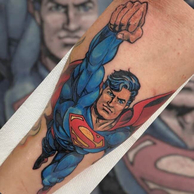 Colour Cartoon Comic Book Superman In Blue Suit Red Cape Flying Pose Forearm Tattoo