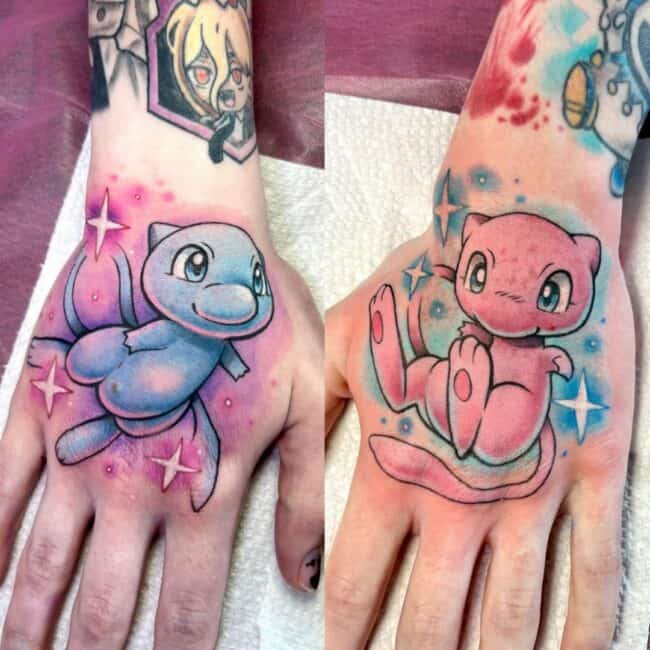 Colour Anime Cartoon Mew and Mewtwo Floating with Tail Curled Paws Outstretched Surrounded Pink Purple Blue Nebulous Shapes White Stars Left Right Hand Wrist Tattoo